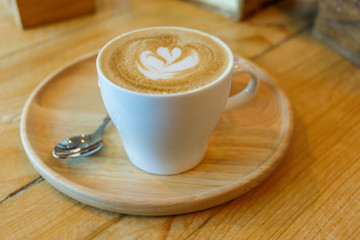 cup of coffee with heart pattern in a white cup on wooden backgr