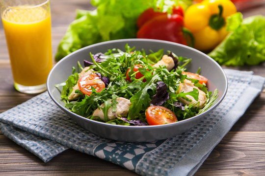 Fresh salad with chicken, tomatoes, arugula, mesclun, basil and orange juice on a cloth napkin, on wooden table