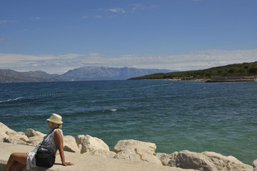 Women sitting on a pir looking out over the sea, blue sky in background, picture from Island Brac in Croatia.