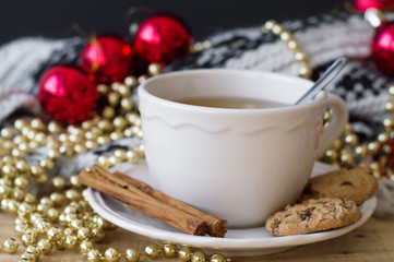 Green tea with cinnamon and chocolate cookies and christmas decoration. Red christmas ball, golden chain with beads and knitted blanket. Christmas breakfast
