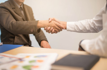 Fototapeta premium Business partners handshaking over business objects on workplace. Business people shaking hands in office.