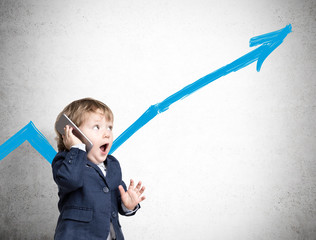 A toddler is on the phone near a concrete wall with a graph