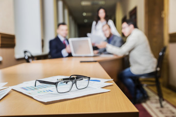 financial chart near dollars seen by unfocused glasses ( colleagues meeting to discuss their future financial plans only silhouettes being viewed )