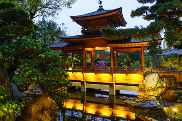 Fototapeta premium Illuminated wooden pagoda by the pond with trout in Nan Lian Garden at Diamond Hill in Hong Kong twilight scenery