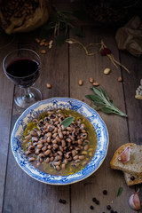 fagioli lessati conditi con olio, salvia e aglio; bicchiere di vino rosso e sacchetti con fagioli sullo sfondo