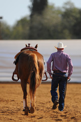 The rear view of a rider in cowboy hat and his horse going away