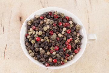 Grains of colorful pepper in the cup  on wooden plank