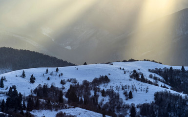 A rays of sunshine at sunset in the winter mountains covered with snow.