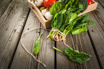 Fresh raw organic vegetables on a rustic wooden table in basket: spinach, broccoli, Brussels sprouts, tomatoes, mushrooms, champignons. 