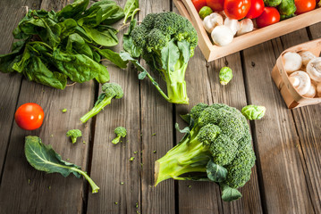 Fresh raw organic vegetables on a rustic wooden table in basket: spinach, broccoli, Brussels sprouts, tomatoes, mushrooms, champignons. 