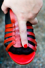 Red sandals wearing on his leg. Women's hand rests on the leg.
