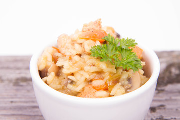 Risotto with chicken, bell pepper, onion, portobello and parsley on a wooden background