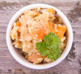 Risotto with chicken, bell pepper, onion, portobello and parsley on a wooden background