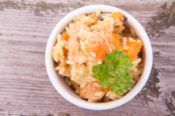 Risotto with chicken, bell pepper, onion, portobello and parsley on a wooden background
