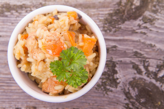 Risotto with chicken, bell pepper, onion, portobello and parsley on a wooden background