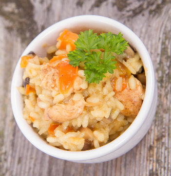 Risotto with chicken, bell pepper, onion, portobello and parsley on a wooden background