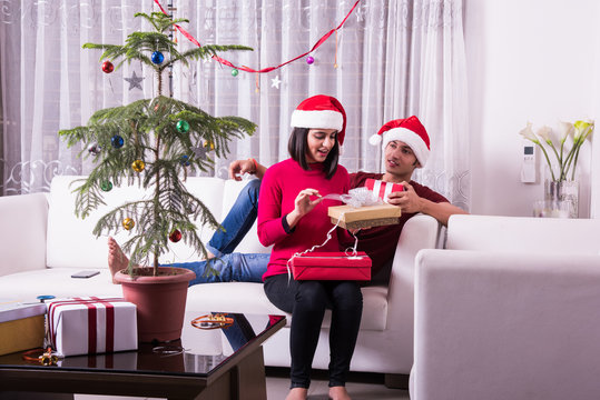 Merry Christmas. Young Indian Or Asian Couple Celebrating Christmas At Home With Surprise Gift Boxes