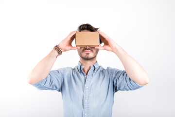 studio shot of a young, professional man looking through cardboard virtual reality (VR) headset, isolated on white