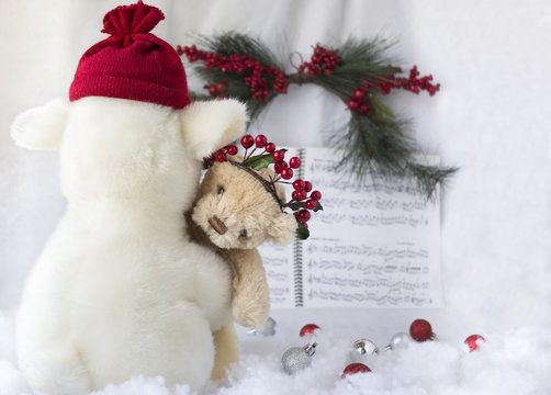 horizontal christmas image of stuffed toy lamb with hat holding  toy brown bear looking over the lambs shoulder at camera with green fern and cranberry and sheet music in the back on white background