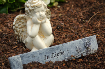 little angel sculpture decorate in small garden with flowers in front it and a sign - in love - in German