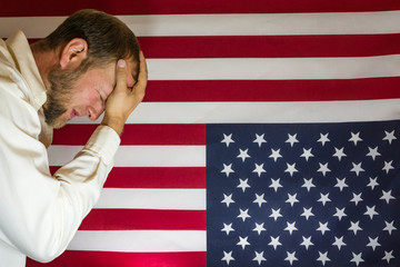 Presidential election disbelief.  Man with head in hands in front of an upside down American flag. ...