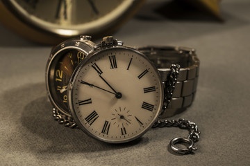 Old pocket watch and modern watch in close-up view with old wall clock in background