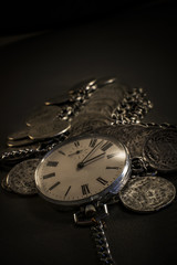 Old pocket watch in dark environment with coin jewelers 