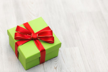 Green gift box with red ribbon bow laid on a wooden background