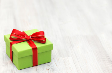 Christmas green gift box with red ribbon bow laid on a wooden ba