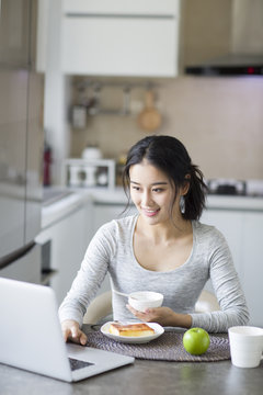 Young woman using laptop while having breakfast