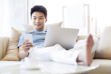 Young man using laptop and smart phone on the sofa
