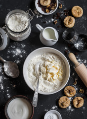 Baking background. Ingredients for preparation of the cookies with dried figs and raisins. On a dark background, top view. Flat lay