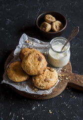 Simple rustic homemade cookies with dried figs and raisins and greek yogurt on a wooden cutting board on dark background