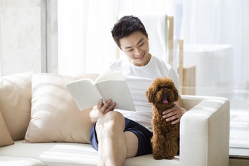 Young man reading with a pet poodle on the sofa