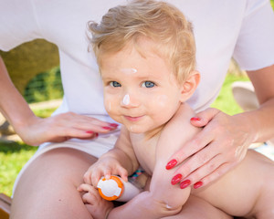 Child with cream on his face lying on Mother's legs after a bath. © robertobinetti70