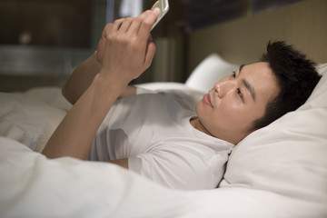 Young man using smart phone on bed