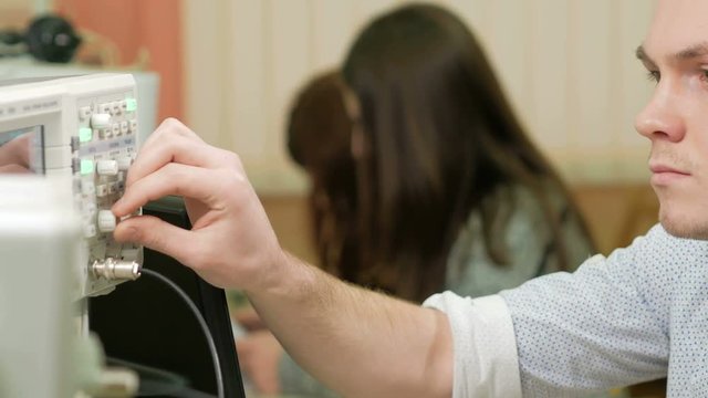 Young woman engineer student working with a man in the laboratory with an electrical measuring equipment. They carefully rotate the clock and recorded data