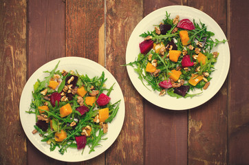 Fall salad with greens, arugula, walnuts, beetroot and roasted squash, pumpkin on wooden background