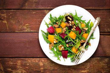 Fall salad with greens, arugula, walnuts, beetroot and roasted squash, pumpkin on wooden background