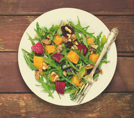 Fall salad with greens, arugula, walnuts, beetroot and roasted squash, pumpkin on wooden background