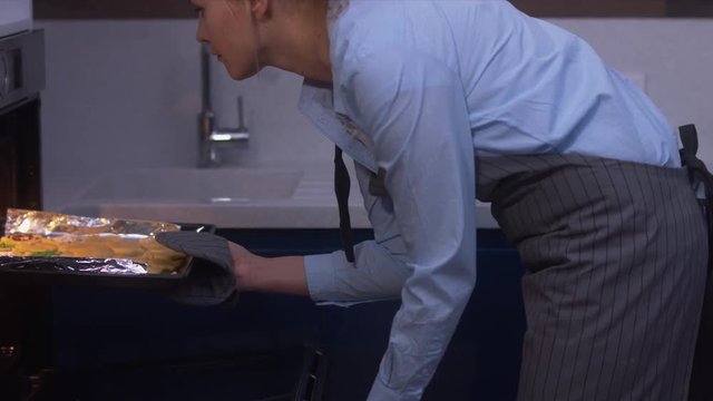RL DOLLY Young attractive female putting cooking pan with dough for cookies into the oven. 4K UHD RAW edited footage