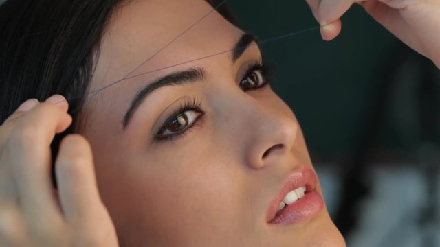 CU woman plucking eyebrows with thread