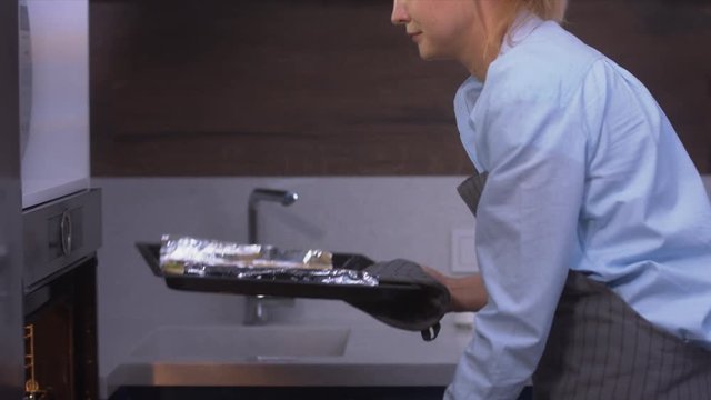 RL DOLLY Young attractive female putting cooking pan with dough for cookies into the oven. 4K UHD RAW edited footage