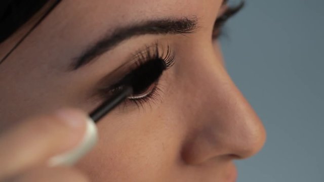 ECU Young woman applying mascara to eyelashes, studio shot