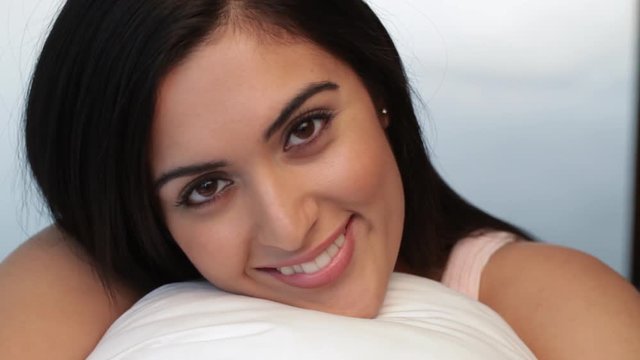 CU Portrait of young woman hugging pillow and smiling