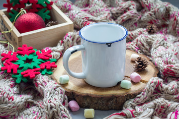 Obraz na płótnie Canvas Empty enamel mug, prepared for hot chocolate with marshmallow, on tree cut, warm scarf on background, horizontal