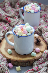 Homemade hot chocolate topped with marshmallow in enamel mug, warm scarf on background, vertical