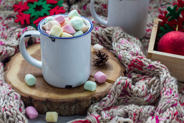 Homemade hot chocolate topped with marshmallow in enamel mug, warm scarf on background, horizontal