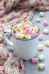Homemade hot chocolate topped with marshmallow in enamel mug, warm scarf on background, vertical