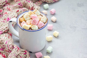 Homemade hot chocolate topped with marshmallow in enamel mug, warm scarf on background, horizontal, copy space